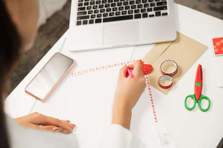 Close up female hands making greeting card for New Year and Christmas 2021 for friends or family, scrap booking, DIY. Writing a letter with best wishes, design her homemade card. Holidays, celebration.の写真素材