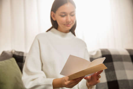 Woman opening, recieving greeting card for New Year and Christmas 2021 from friends or family. Reading a letter with best wishes, looks happy, cheerful, smiling, opening envelope. Holidays, celebration.の写真素材