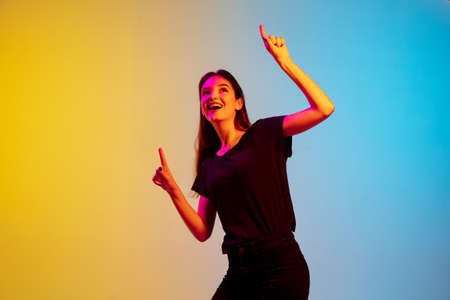 Pointing, laughting. Young caucasian womans portrait on gradient blue-yellow studio background in...