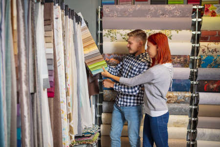 Palette. Couple choosing textile at home decoration store, shop. Making of home interior design during quarantine. Happy man and woman, young family look dreamful, cheerful choosing materials.の写真素材