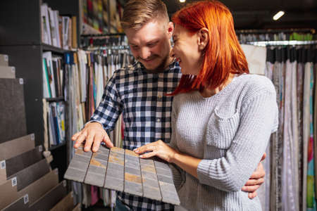 Cover. Couple choosing textile at home decoration store, shop. Making of home interior design during quarantine. Happy man and woman, young family look dreamful, cheerful choosing materials.の写真素材