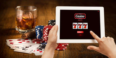 Online gambling, casino concept. Hand holding device with lottery, casino cover. Playing dips and cards on table on the background. Poker, bookmaking, gaming, modern technologies, business and finance.の写真素材
