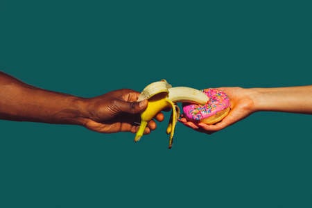 Hands with banana and donut. Modern art collage in pop-art style. Hands isolated on trendy colored background with copyspace, contrast. Modern design with copyspace for advertising. Trendy colors.の写真素材