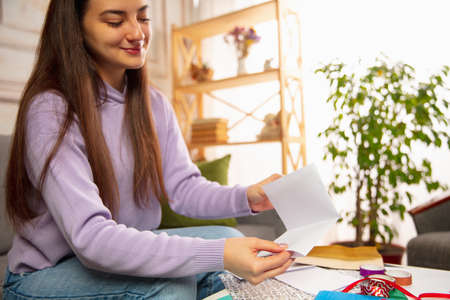 Comfortable. Woman writing letter, greeting card for New Year and Christmas 2021 for friends or family sitting at home with laptop. Holidays, celebration. Looks cheerful, happy, careful.の写真素材