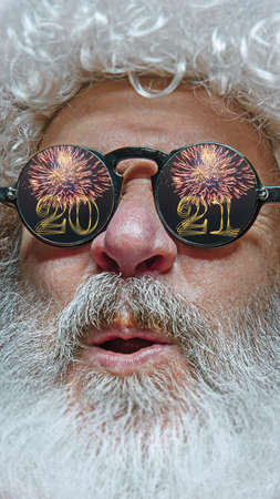 Close-up shot of Santa Claus in stylish glasses with a reflection of 2021 Happy New Year and salute....