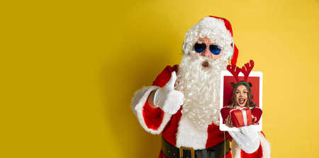 Greeting flyer for ad. Concept of Christmas, 2021 New Years party, winter mood, holidays. Copyspace, postcard. Santa Claus holding tablet with beautiful woman holding gifts on its screenの写真素材