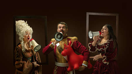 Medieval people as a royalty persons in vintage clothing shouting with loudspeaker on dark...