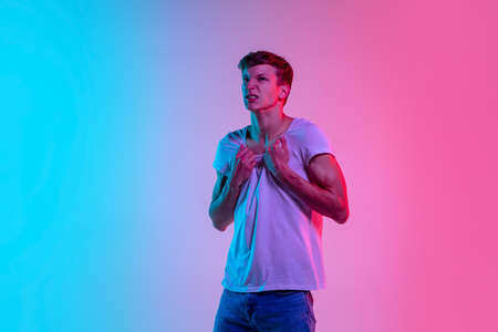 Crazy angry, mad. Young caucasian mans portrait on gradient blue-pink studio background in neon light. Concept of youth, human emotions, facial expression, sales, ad. Beautiful model in casual.の写真素材