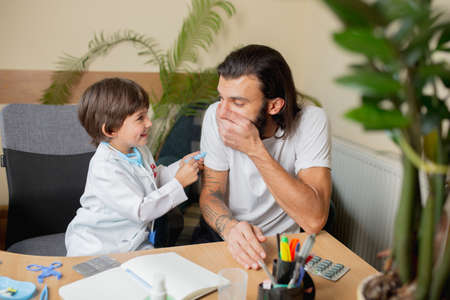 Little boy playing pretends like doctor examining a man in comfortabe medical office. Healthcare,...