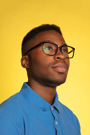 Wearing stylish eyewear. Young african-american mans portrait isolated on yellow studio background,...