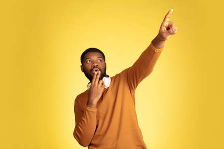 Pointing, choosing. Young african-american mans portrait isolated on yellow studio background,...