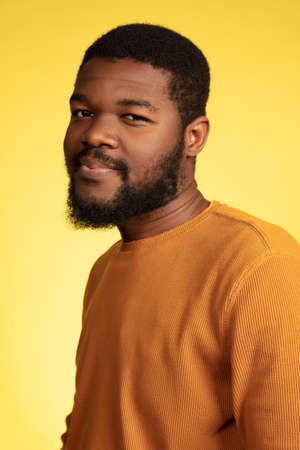 Calm, thoughtful. Young african-american mans portrait isolated on yellow studio background, facial expression. Beautiful male model, monochrome, copyspace. Concept of human emotions, sales, ad.の写真素材