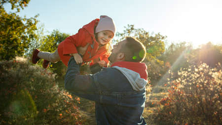 Flying high. Happy father and little cute daughter walking down the forest path in autumn sunny day....