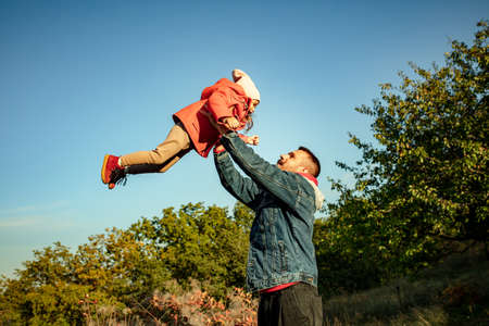 Flying high. Happy father and little cute daughter walking down the forest path in autumn sunny day....