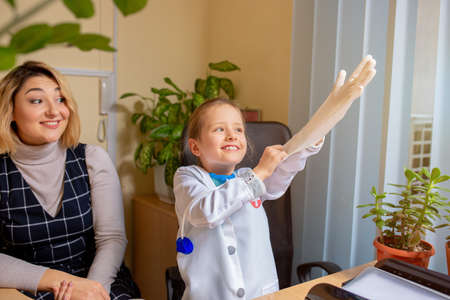 Little girl playing pretends like paediatrician doctor examining a patient in comfortabe medical office. Healthcare, childhood, medicine, education concept. Having fun while wearing glovesの写真素材