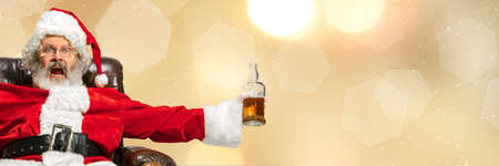 Greeting flyer for ad. Concept of Christmas, 2021 New Years, winter mood, holidays. Copyspace, postcard. Santa in traditional costume drinking isolated on golden bokeh background. Horizontal flyerの写真素材