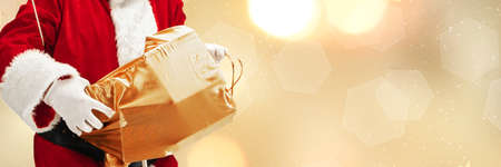Greeting flyer for ad. Concept of Christmas, 2021 New Years, winter mood, holidays. Copyspace, postcard. Santa in traditional costume carrying gifts isolated on golden bokeh background. Horizontalの写真素材