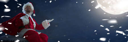 Greeting flyer for ad. Concept of Christmas, 2021 New Years, winter mood, holidays. Copyspace, postcard. Santa in traditional costume carrying gifts with midnight on background, confetti. Horizontalの写真素材