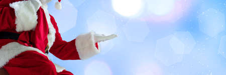 Greeting flyer for ad. Concept of Christmas, 2021 New Years, winter mood, holidays. Copyspace, postcard. Santa in traditional costume showing, pointing on blue bokeh background. Horizontalの写真素材