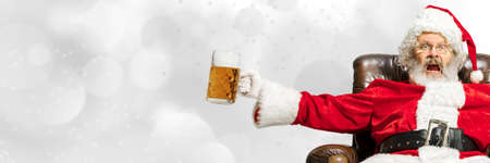 Greeting flyer for ad. Concept of Christmas, 2021 New Years, winter mood, holidays. Copyspace, postcard. Santa in traditional costume drinking beer isolated on white bokeh background. Horizontalの写真素材