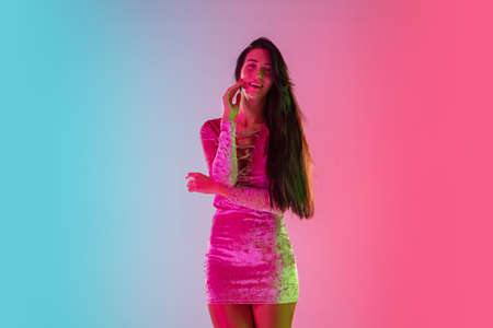 Attractive. Beautiful seductive girl in fashionable dress, outfit on gradient pink-blue background in neon light. Half-length portrait. Copyspace for ad. Summer, fashion, beauty, emotions concept.の写真素材