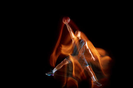 Time to win. Young east asian basketball player in action and motion jumping in mixed light over dark studio background. Concept of sport, movement, energy and dynamic, healthy lifestyle.の写真素材