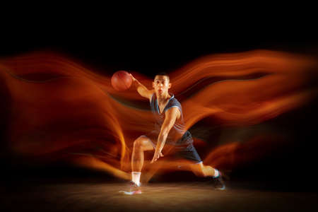 Leadership. Young east asian basketball player in action and motion jumping in mixed light over dark studio background. Concept of sport, movement, energy and dynamic, healthy lifestyle.の写真素材