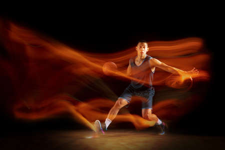 Movement. Young east asian basketball player in action and motion jumping in mixed light over dark...