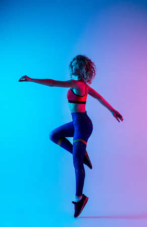 Training. Young sportive woman training isolated on gradient blue-pink studio background in neon light. athletic and graceful. Modern sport, action, motion, youth concept. Beautiful female practicing.の写真素材