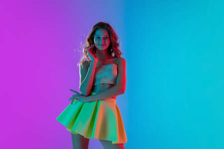 Emotions. Beautiful seductive girl in fashionable yellow skirt on gradient pink-blue neon background. Half-length portrait. Copyspace for ad. Flyer design. Summer, fashion, human emotions concept.の写真素材