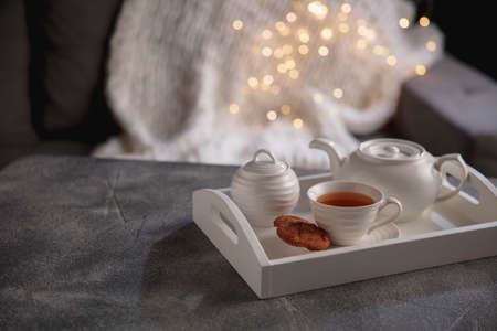 White tea set and cakes on wooden grey table. White wooden tray with cups, teapot and garland lights. The concept of home atmosphere, romantic date, winter, home comfort, Christmas or New Year.の写真素材