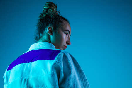 Posing. Professional female judoist in white judo kimono practicing and training isolated on blue...
