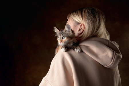 A small purebred kitten sitting on the shoulder of a young woman isolated on colored background....