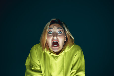 Screaming. Portrait of young crazy scared and shocked caucasian woman isolated on dark background....