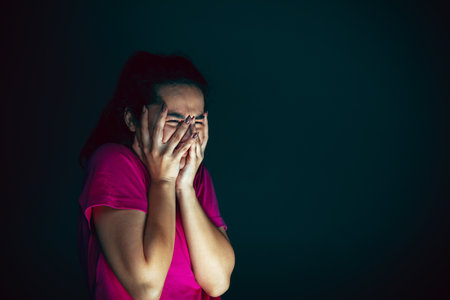Crying. Portrait of young crazy scared and shocked caucasian woman isolated on dark background. Copyspace for ad. Bright facial expression, human emotions concept. Looking horror on TV, cinema.の写真素材