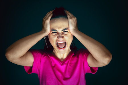 Holding head. Portrait of young crazy scared and shocked caucasian woman isolated on dark background. Copyspace for ad. Bright facial expression, human emotions concept. Looking horror on TV, cinema.の写真素材