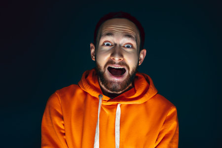 Screaming. Portrait of crazy scared and shocked caucasian man isolated on dark background. Copyspace for ad. Bright facial expression, human emotions concept. Watching horror on TV, cinema.の写真素材