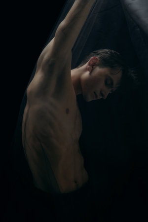 Overcome. Graceful classic ballet male dancer isolated on white studio background. Man in minimalistic black cloth looks graceful, inspired. The grace, artist, movement, action and motion concept.の写真素材