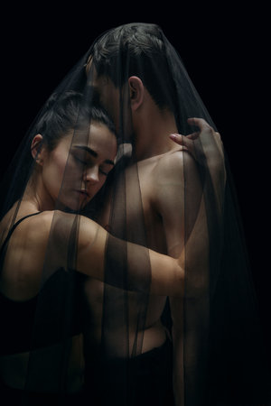 Together. Graceful classic ballet dancers isolated on black studio background. Couple in minimalistic dark cloth look graceful, inspired. The grace, artist, movement, action and motion concept.の写真素材