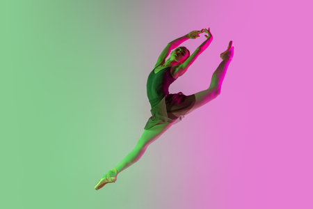Flying. Young and graceful ballet dancer isolated on gradient pink-green studio background in neon. Art, motion, action, flexibility, inspiration concept. Flexible ballerina, weightless jumps.の写真素材