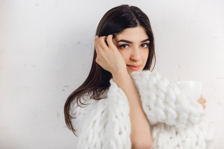 Touch. Portrait of beautiful brunette woman in comfortable soft longsleeve isolated on white studio background. Home comfort, human emotions, facial expression, winter mood concept. Copyspace.の写真素材