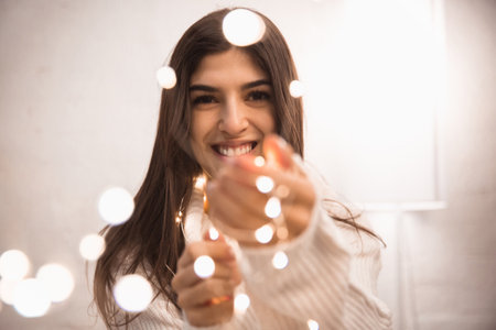 Bokeh. Portrait of beautiful brunette woman in comfortable soft longsleeve isolated on white studio background. Home comfort, human emotions, celebration, holidays, winter mood concept. Copyspace.の写真素材