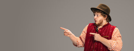 Pointing, flyer. Happy smiling man dressed in traditional Austrian or Bavarian costume gesturing...