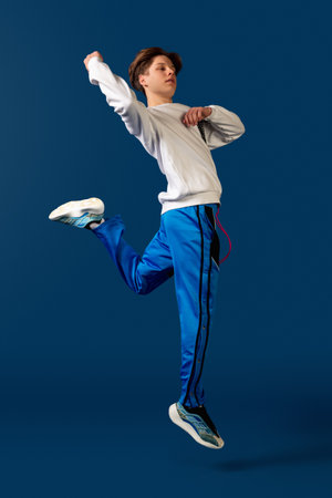 Jumping. Old-school fashioned young man dancing isolated on blue studio background. Artist fashion, motion and action concept, youth culture, fashion returning. Young caucasian curly boy.の写真素材