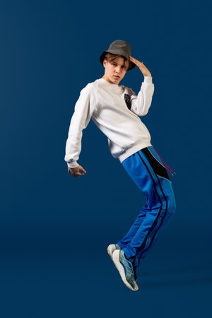 Balancing. Old-school fashioned young man dancing isolated on blue studio background. Artist fashion, motion and action concept, youth culture, fashion returning. Young caucasian curly boy.の写真素材