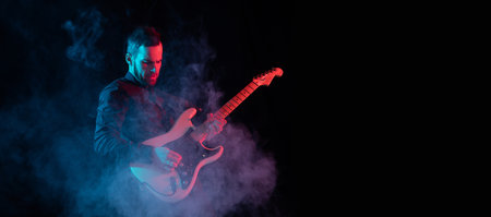 Flyer. Silhouette of young male guitarist isolated on blue-pink gradient studio background in neon. Beautiful shadow in action, performing. Concept of human emotions, expression, ad, music, art.の写真素材