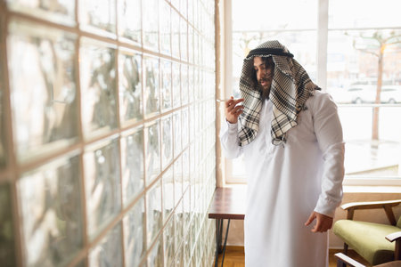 Message. Arabian businessman working in office, business centre using device, gadget. Modern saudi lifestyle. Man in traditional wear and scarf looks confident, busy, handsome. Ethnicity, finance.の写真素材