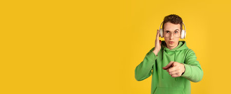 Choosing. Caucasian young mans portrait on yellow studio background. Beautiful male model in green outfit with cellphone. Concept of human emotions, facial expression, sales, ad, beauty. Flyer.の写真素材