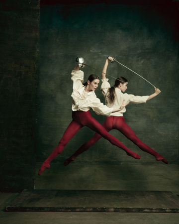 Fight. Two young female ballet dancers like duelists with swords on dark green background. Caucasian models dancing together. Ballet and contemporary choreography concept. Creative art photo.の写真素材