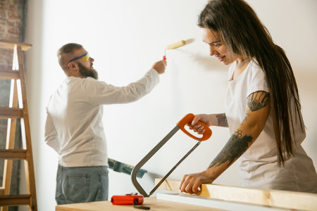 Young couple, family doing apartment repair together themselves. Married man and woman doing home makeover or renovation. Concept of relations, moving, love. Painting wall, preparing equipmentの写真素材